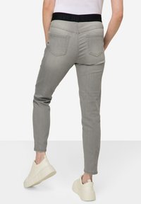 Jeans skinny de mezclilla gris con una cinturilla elástica negra y diseño de cinco bolsillos, combinados con zapatillas de plataforma blancas. Textura suave.