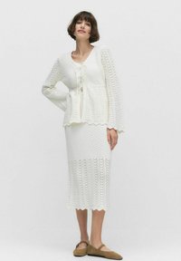 Biały dzianinowy zestaw składający się z topu z fakturowanym peplum i wiązaniem oraz sp ódnicy o średniej długości z falbaniastymi krawędziami.