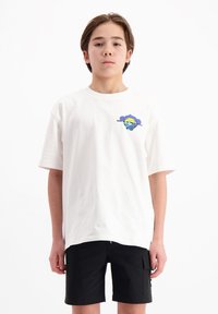 Witte katoenen t-shirt met korte mouwen, voorzien van een kleurrijk grafisch ontwerp op de linkerkant van de borst. Gepaarde met zwarte shorts.