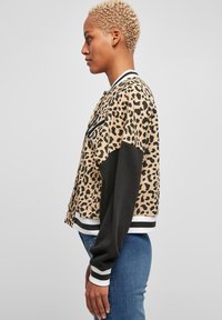 Bomber jakna s leopard uzorkom i crnim rukavima, rebrasti prugasti rub i ovratnik. Napravljena od mekanog materijala sa skraćenim dizajnom.