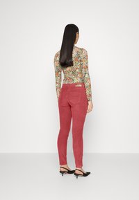 Pantaloni di velluto a coste rossi con una vestibilità slim, abbinati a un body floreale a maniche lunghe aderente. Sul retro ci sono due tasche e un'etichetta con il marchio.