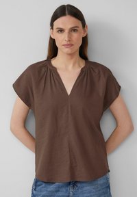 Blouse marron à manches courtes avec un col en V et des fronces au niveau du col, en tissu doux, associée à un short en denim décontracté.