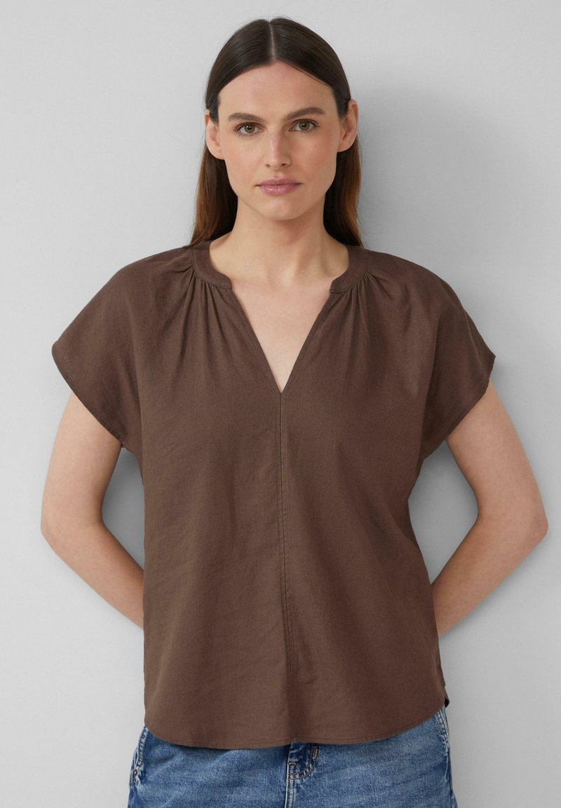 Blouse marron à manches courtes avec un col en V et des fronces au niveau du col, en tissu doux, associée à un short en denim décontracté.