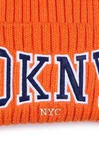 Bonnet en tricot orange avec "DKNY" en texte bleu marine et blanc, et une petite étiquette "NYC" dorée en bas. Design à nervures texturées.