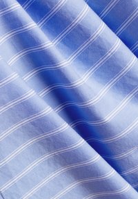 Tessuto azzurro chiaro con sottili righe bianche, caratterizzato da una superficie liscia e strati diagonali. Il motivo è composto da linee curve e fini.