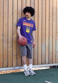 Violet basketbola krekls ar uzrakstu "NUGGETS" un numuru "15" gradienta dzeltenā-oranžā krāsā. Pelēkas šortus un kustību sensorus apavus. Tur rokās basketbola bumbu.