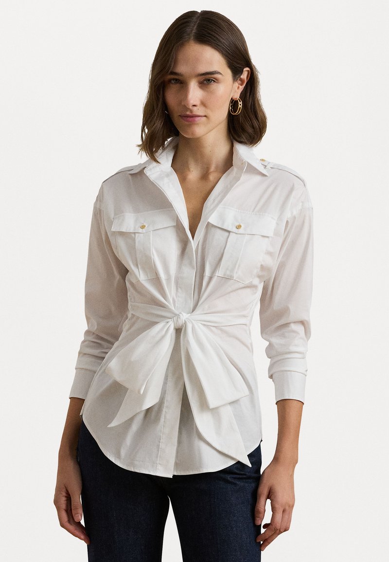 Balts krekls ar garām piedurknēm, divām krūšu kabatām, mezgla priekšpusi un zelta akcentiem uz pleciem.