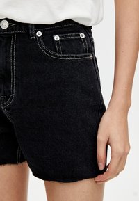 Zwarte denim shorts met een rafelige zoom, contrasterende witte stiksels en zilveren knoopaccenten. Voorkringen zichtbaar, aansluitend ontwerp.