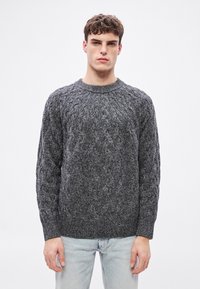 Pelēks džemperis ar kabeljaušanas rakstu, apaļu izgriezumu un garām piedurknēm, ar teksturētiem rakstiem un brīvu pieguļumu. Kombinēts ar gaiši zilām džinsa biksēm.