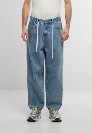 Lyseblå denimbukser med løs passform, med snor i livet og to frontlommer. Brukt med grå sneakers.