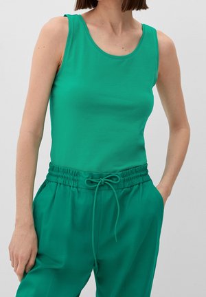 Zielona bezrękawnikowa bluzka wykonana z gładkiego, elastycznego materiału, zestawiona z dopasowanymi luźnymi spodniami z elastycznym paskiem w talii i sznurkiem.