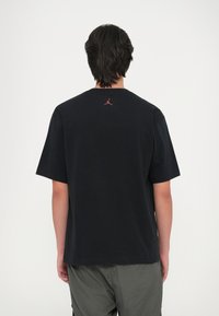 Musta puuvillane t-särk lühikeste varrukatega, seljal väike punane Jordani logo, ümar kaelus ja mugav lõige.