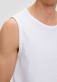 White sleeveless cotton tank top with a round neck and smooth texture, showing a close-up of the shoulder and upper arm.