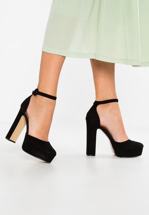 Zwarte suède hoge hakken met een platform voorkant, enkelbandje, open hak en een ronde neus. Zwart en beige kleurcontrast.