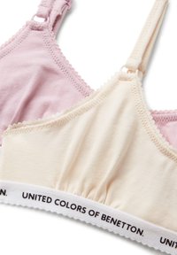 Dos sujetadores de tela suave en rosa claro y crema, con tirantes ajustables y bandas elásticas blancas con el texto "United Colors of Benetton".
