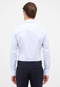 Lichtblauw overhemd met lange mouwen, een puntige kraag, knoopsluitingen bij de manchetten en een gladde textuur, gecombineerd met donkere broeken met achterzakken.