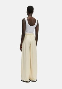 Wijdvallende broek in lichtcrème stof, met een elastische tailleband en zwart scalloped trim aan de zoom. Achteraanzicht weergegeven.