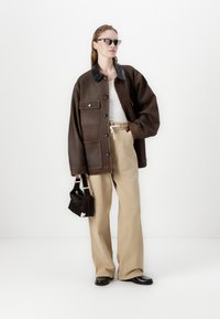 Brun oversized jakke med sort skinnkrage, hvit topp, beige vide bukser og liten svart veske med hvit detalj. Flate sko.