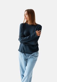Ciemnogranatowy sweter z długimi rękawami, okrągłym dekoltem i miękką fakturą, zestawiony z jasnoniebieskimi dżinsami. Prosty fason, bez widocznych wzorów.