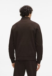 Hnedá mikina s dlhým rukávom z textúrovanej látky, s rebrovanými manžetami a vysokým golierom, s voľným strihom a rovnomerným zakončením.