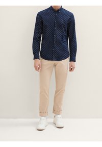 Camicetta blu con bottoni e stampa di stelle bianche, abbinata a chinos beige chiari e sneaker bianche. Presenta un colletto e chiusura a bottoni.