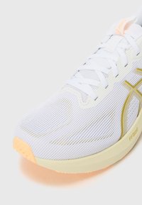 White running shoe with mesh upper, featuring yellow accents, thin laces, and a light orange sole. Design prioritizes breathability and comfort.