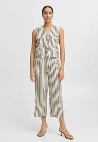 Combinaison en lin beige avec des rayures verticales foncées. Elle présente un design sans manches, un col en V, des détails de boutons et un pantalon large à jambes raccourcies.