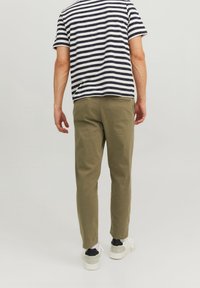 Koszulka w paski z krótkim rękawem w kolorze granatowym i białym, zestawiona z oliwkowozielonymi, zwężanymi spodniami. Model ma na sobie białe i czarne trampki.