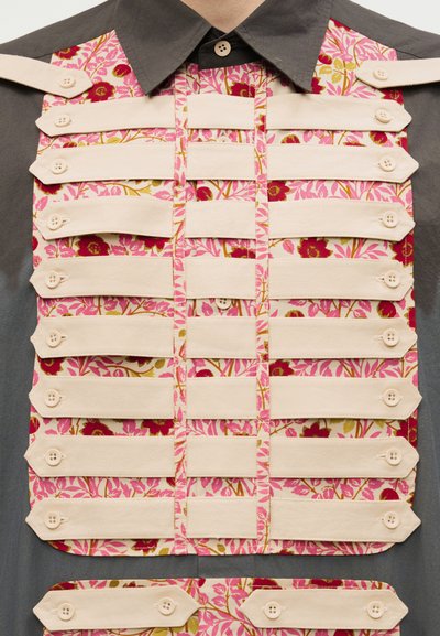 Hall triiksärk roosa lillemustrilise paneeliga, kaunistatud horisontaalsete kreemja värvi kangast ribadega, mis on kinnitatud nööbid.