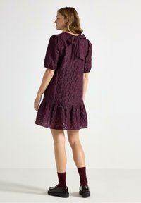 Kort lila spetsklänning med puffärmar och en båndetalj på baksidan, avslutad med en volangkant. Matchad med mörka strumpor och loafers.