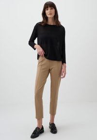 Zwarte langemouwen top met een relaxte pasvorm, gecombineerd met beige tapered broek en zwarte loafers met kwastjes. Eenvoudig, modern ontwerp.