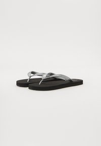 Sorte flip-flops med en teksturert såle, med metallisk sølvfarge på stroppene og et preget logo på en av stroppene. Enkelt design, lett materiale.
