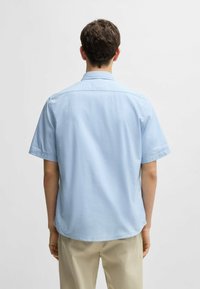 Camicia a maniche corte con colletto in tessuto azzurro chiaro, caratterizzata da una vestibilità rilassata e una texture liscia, con un orlo arrotondato sul retro.