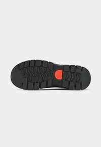 Talpa de pantof sport negru, cu un model de tread robust, cu caneluri proeminente și un accent central roșu. Material din cauciuc texturat, design solid.