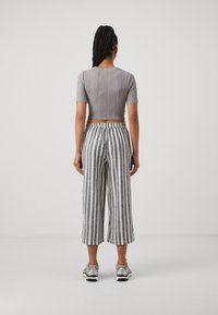 Un crop top gris à côtes associé à un pantalon taille haute à rayures verticales grises et blanches, avec une taille élastique et des baskets.