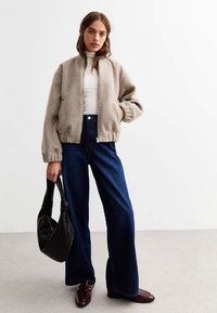 Beige fleece bomberjacka med ribbade manschetter, vit polo, blå vida denimjeans och svart handväska i kombination med bordeauxfärgade loafers.