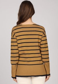 Pull en tricot avec une base moutarde et des rayures horizontales noires, des poignets côtelés et un ourlet arrière légèrement plus long.