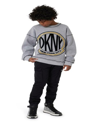 Sweatshirt gris avec logo DKNY noir et jaune, associé à un pantalon cargo noir et des baskets montantes avec un design à motifs.