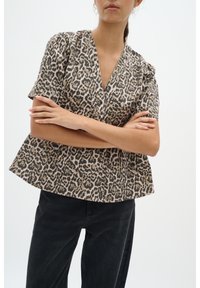 Blůza s krátkými rukávy v leopardím potisku, s výstřihem do V a peplum spodním lemem, vyrobená z lehkého materiálu. Barevná paleta zahrnuje béžové a černé odstíny.