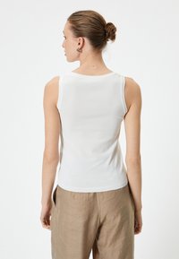 Top blanco sin mangas con escote redondo y dobladillo acanalado. Combinado con pantalones sueltos de color marrón claro, mostrando un atuendo casual.
