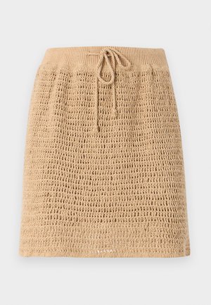 Strikket beige nederdel med et struktureret, åbent vævdesign. Har en snor i taljen for justerbarhed. Kantlinjen er lige.