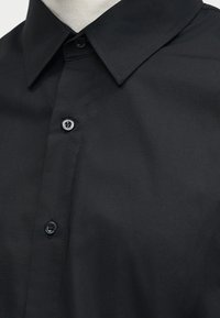 Μαύρο πουκάμισο με κουμπιά και μυτερό γιακά, εμφανιζόμενο σε μανεκέν ή πρόσωπο πάνω σε ουδέτερο φόντο.