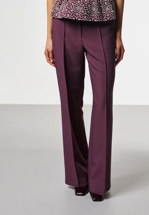 Person wearing high-waisted, wide-leg maroon trousers and a patterned top, standing in a neutral indoor setting. Hands are by their sides.