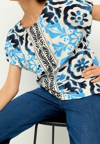 Top holgado de tela ligera con un estampado floral en azul y negro, y con acentos negros contrastantes a lo largo de la costura central.