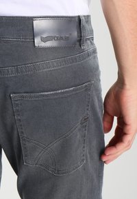 Vaqueros de mezclilla gris con una etiqueta de cuero GAS, un bolsillo trasero único con costuras decorativas y un diseño de corte estándar.