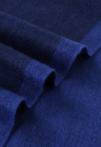 Tessuto di lana blu profondo, caratterizzato da una morbida consistenza con una leggera lucentezza, disposto in pieghe che mostrano variazioni di ombreggiatura e profondità.