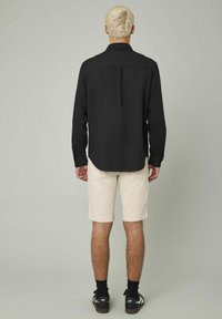 Chemise noire à manches longues avec une coupe regular, associée à un short beige. La chemise arbore un col et des détails de boutons.