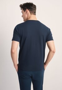 Granatowy, krótki rękaw t-shirt z okrągłym dekoltem, gładką fakturą i luźnym krojem, noszony z delikatnym włożeniem ręki do kieszeni dopasowanych spodni.