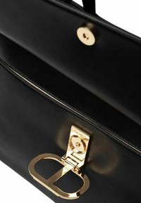 Borsa a mano in pelle nera con una chiusura in tono dorato, texture liscia e cuciture decorative lungo i bordi. Un dettaglio hardware distintivo include un logo.