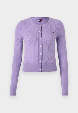 Alyviniai megzti kardiganas su raukšlėtu apykaklė, ilgomis rankovėmis ir mygtukų užsegimu. Jis turi tekstūruotą raštą ir keturis baltus mygtukus.